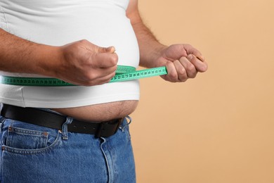 Photo of Overweight man measuring his belly with tape on beige background, closeup. Space for text