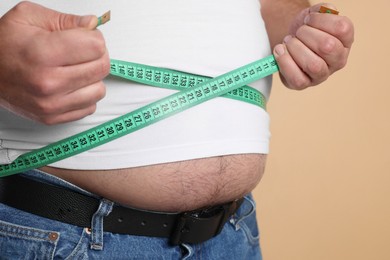 Photo of Overweight man measuring his belly with tape on beige background, closeup