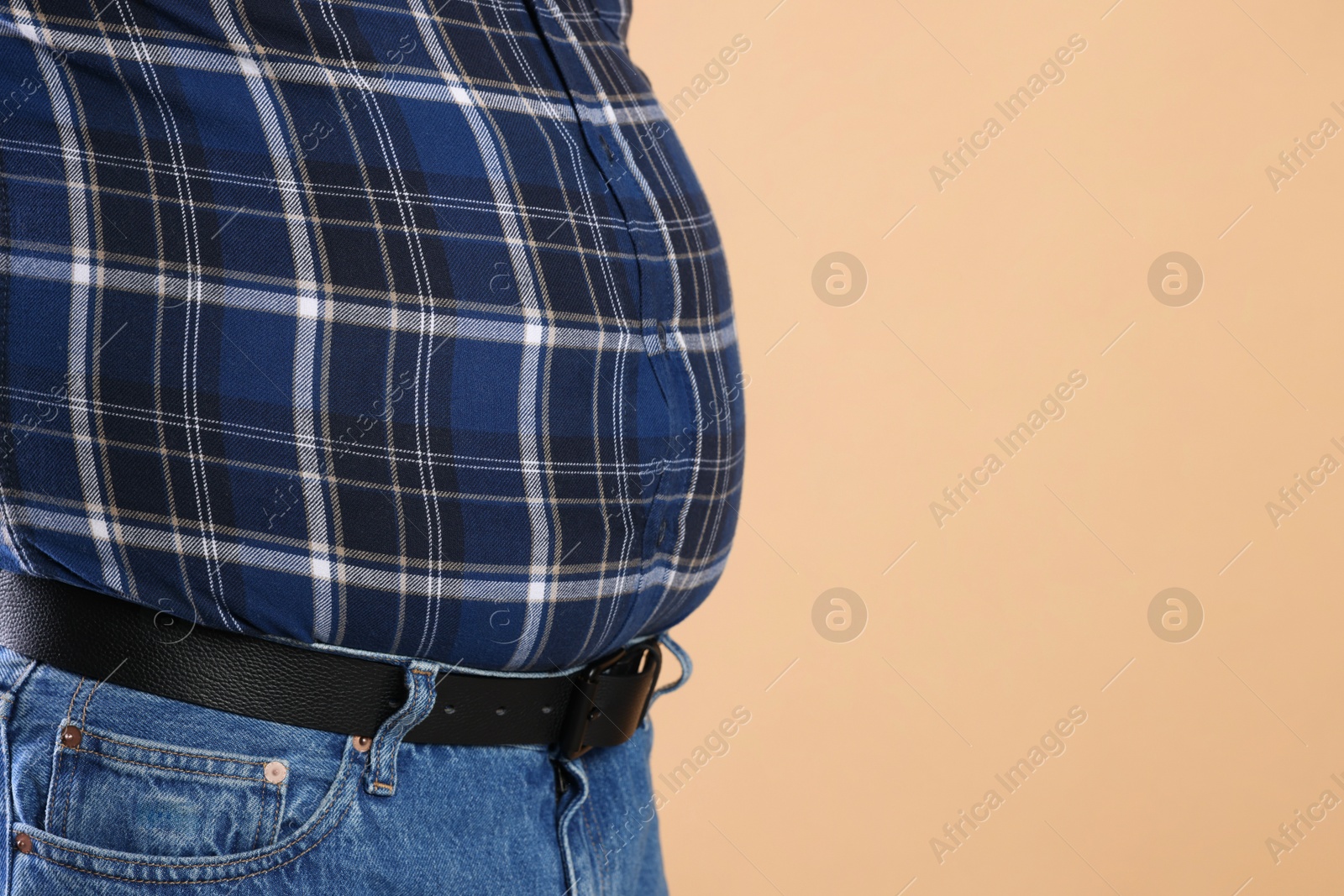 Photo of Overweight man in tight shirt on beige background, closeup. Space for text