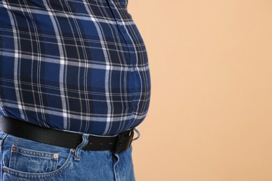 Photo of Overweight man in tight shirt on beige background, closeup. Space for text