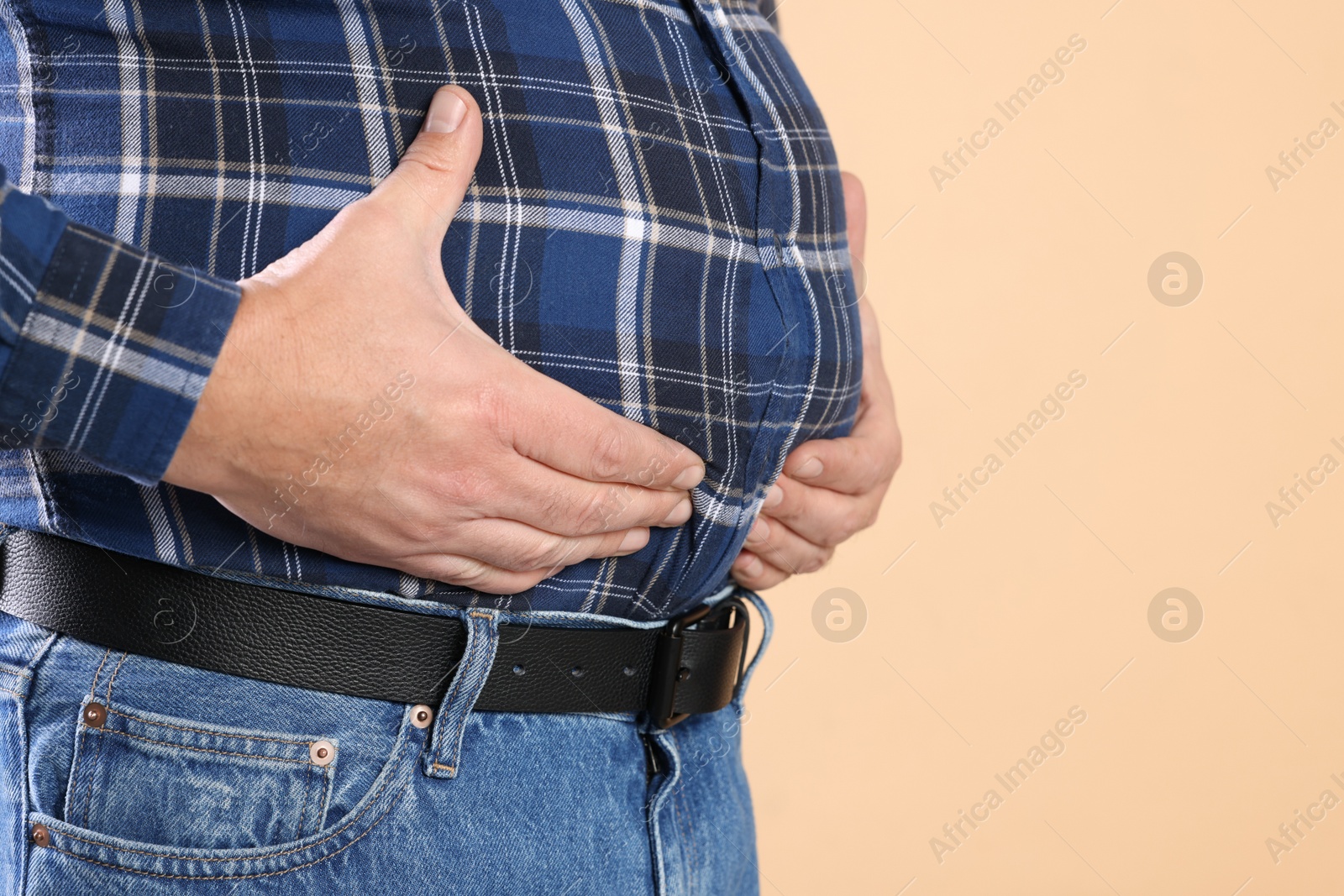 Photo of Overweight man in tight shirt on beige background, closeup. Space for text