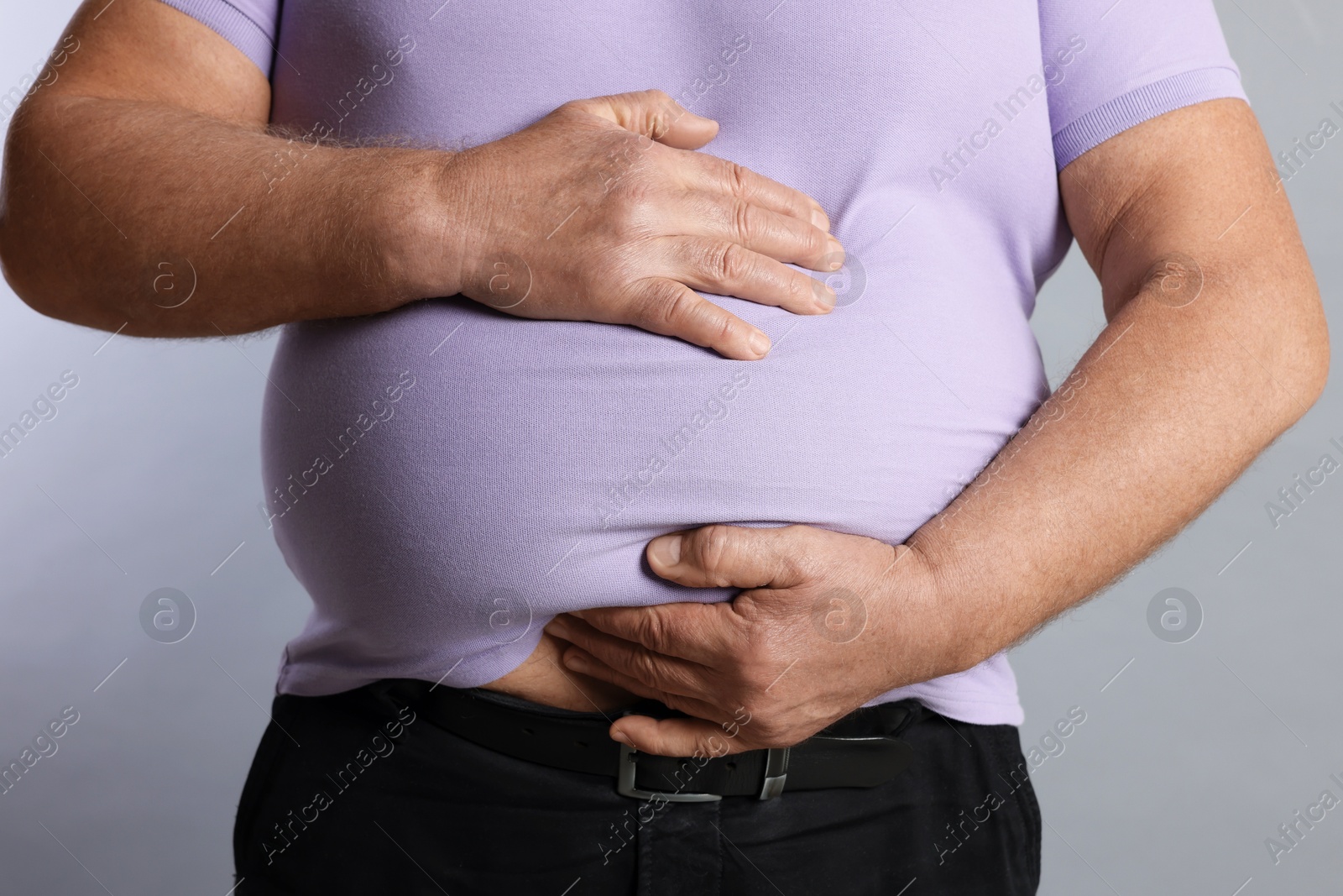 Photo of Overweight man in tight t-shirt on grey background, closeup