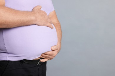 Photo of Overweight man in tight t-shirt on grey background, closeup. Space for text