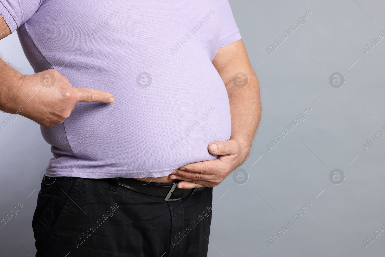 Photo of Overweight man in tight t-shirt on grey background, closeup. Space for text