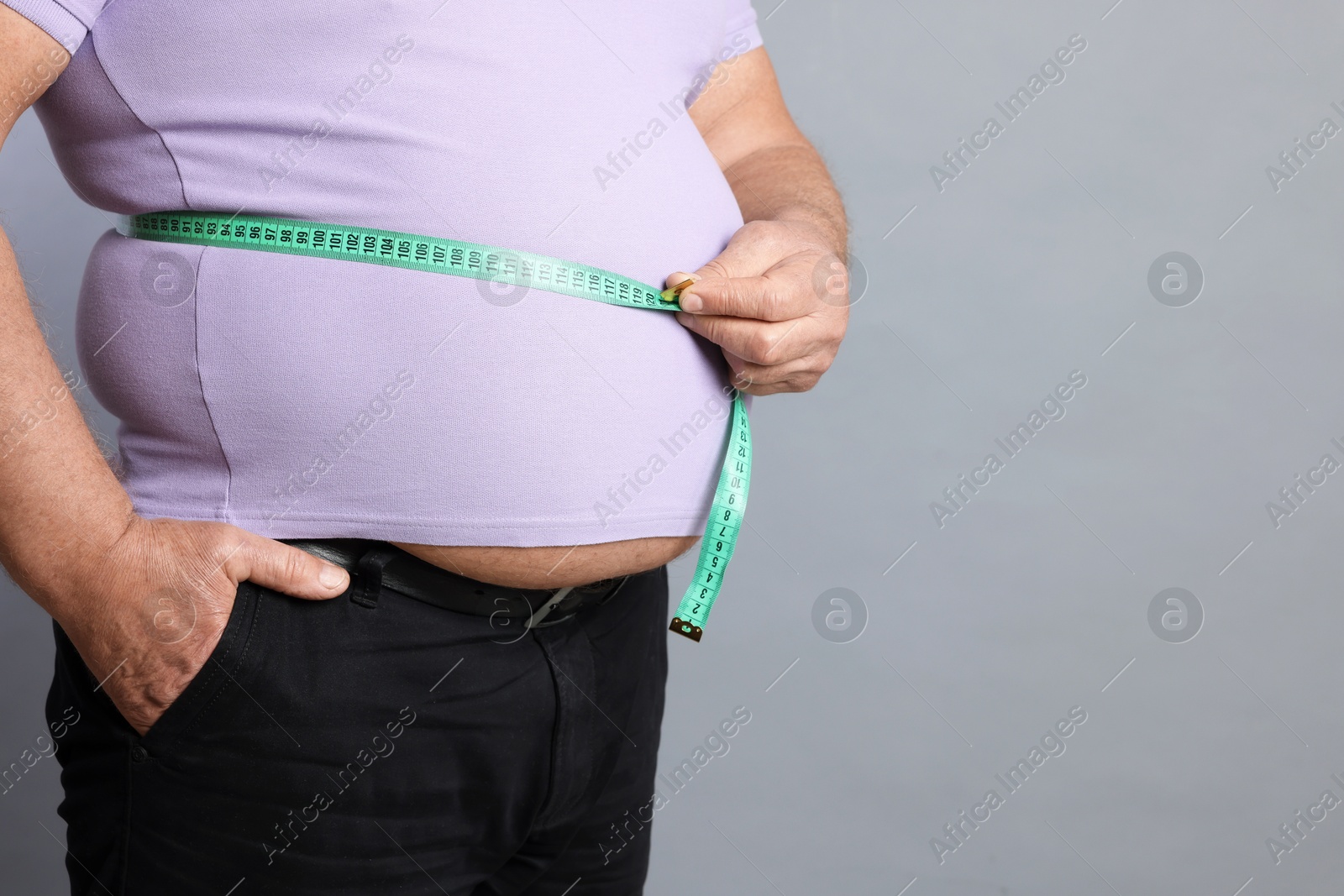 Photo of Overweight man measuring his belly with tape on grey background, closeup. Space for text