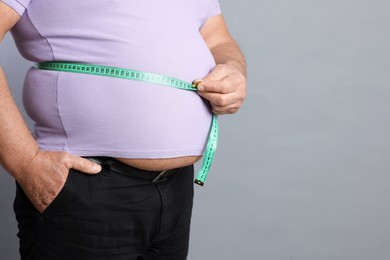 Photo of Overweight man measuring his belly with tape on grey background, closeup. Space for text