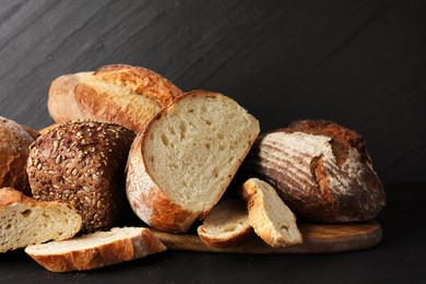 Photo of Whole and cut loafs of bread on black table, closeup