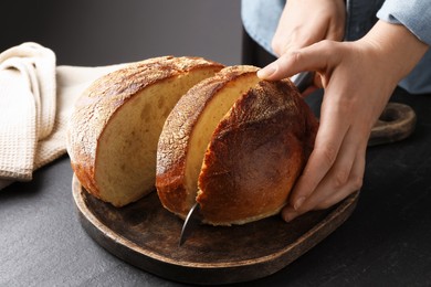 Photo of Woman cutting fresh bread at black table, closeup