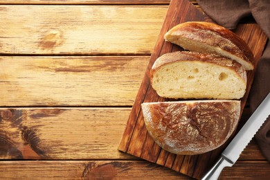 Photo of Cut loaf of fresh bread and knife on wooden table, top view. Space for text