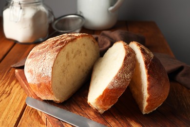 Photo of Cut loaf of fresh bread and knife on wooden table, closeup