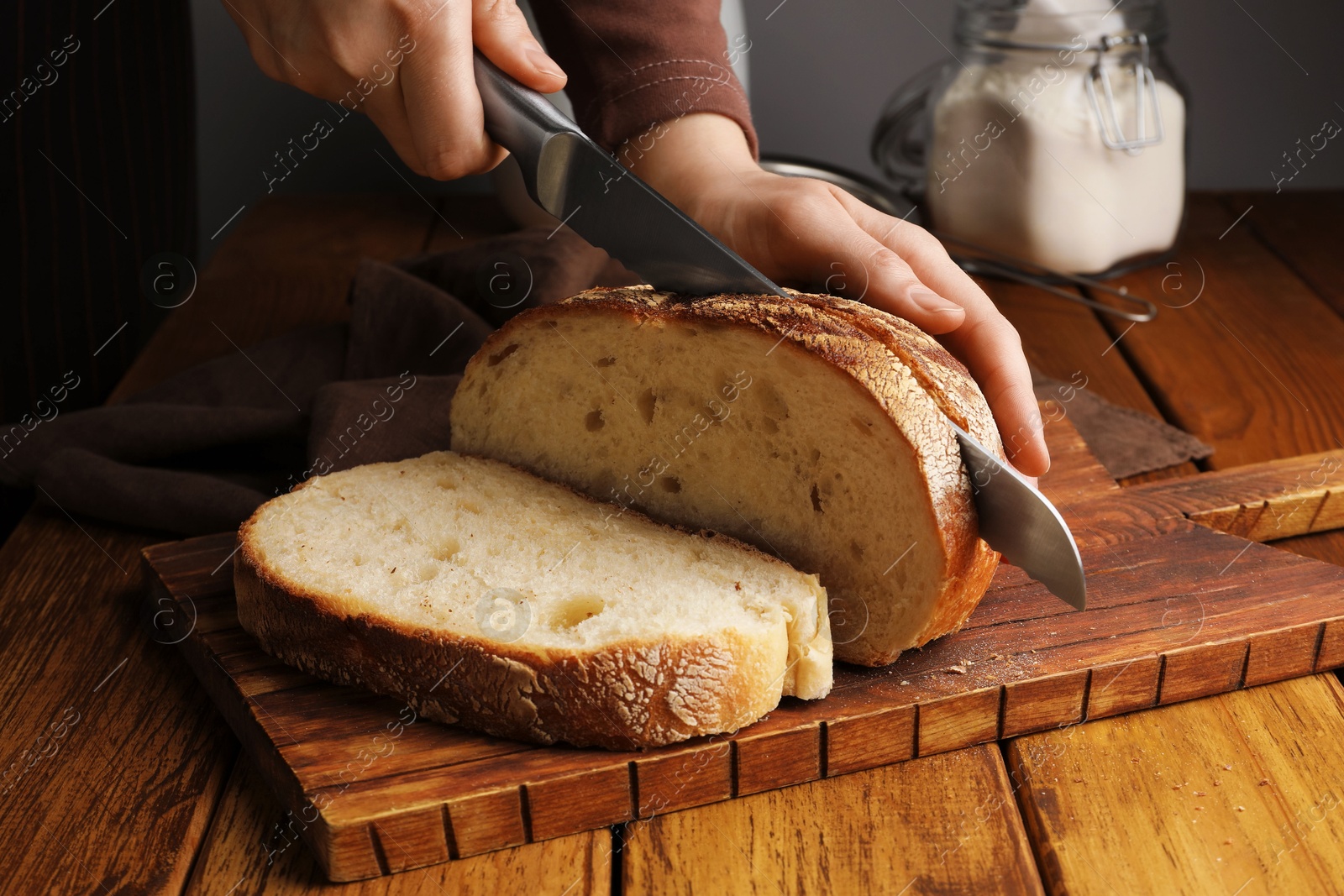 Photo of Woman cutting freshly baked bread at wooden table, closeup