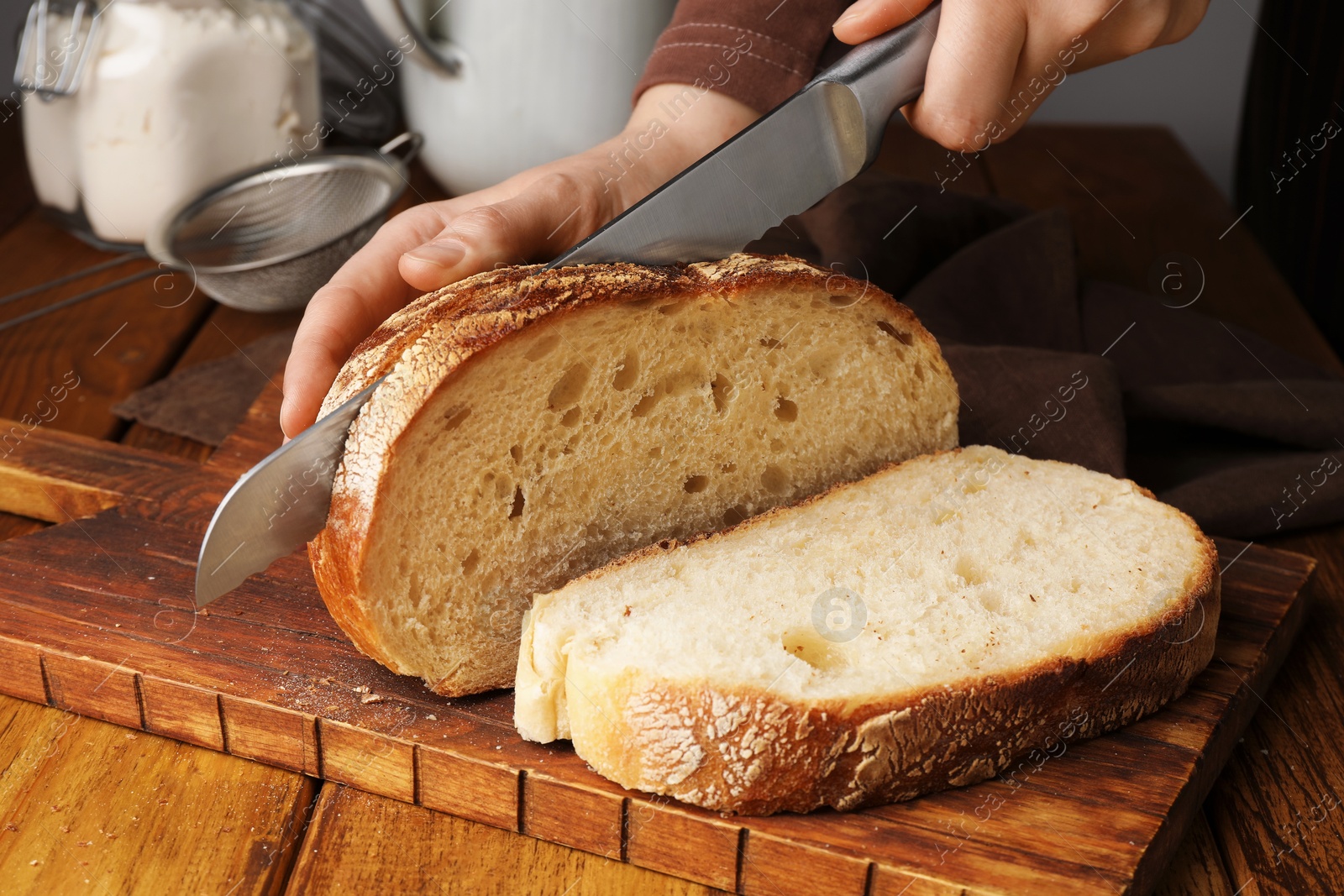 Photo of Woman cutting freshly baked bread at wooden table, closeup