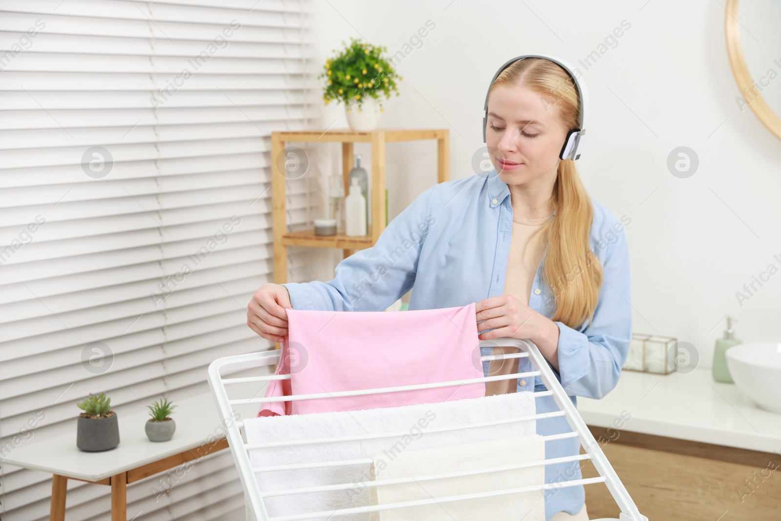 Photo of Woman listening to music while hanging fresh laundry on drying rack at home