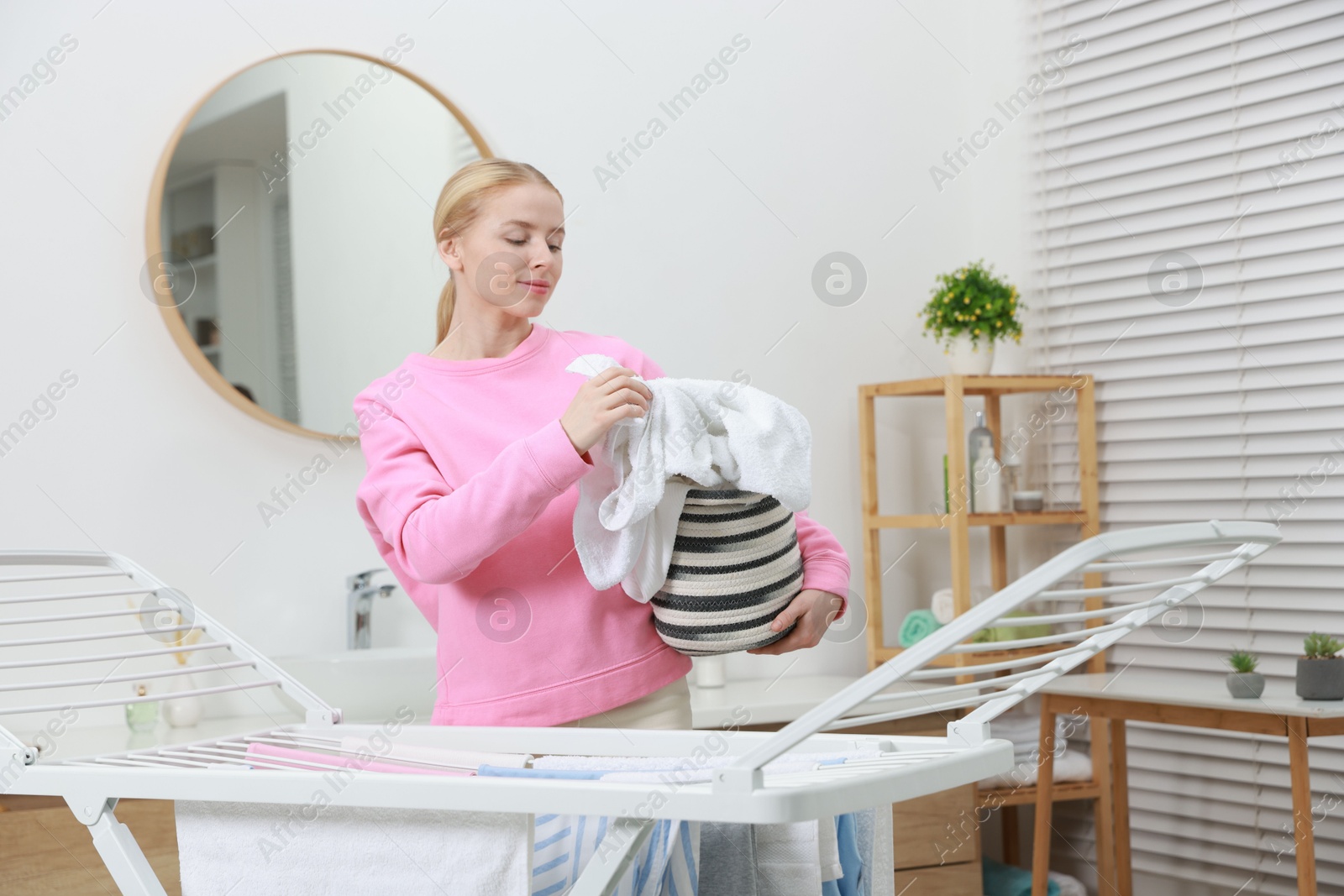 Photo of Beautiful woman hanging fresh clean laundry on drying rack at home