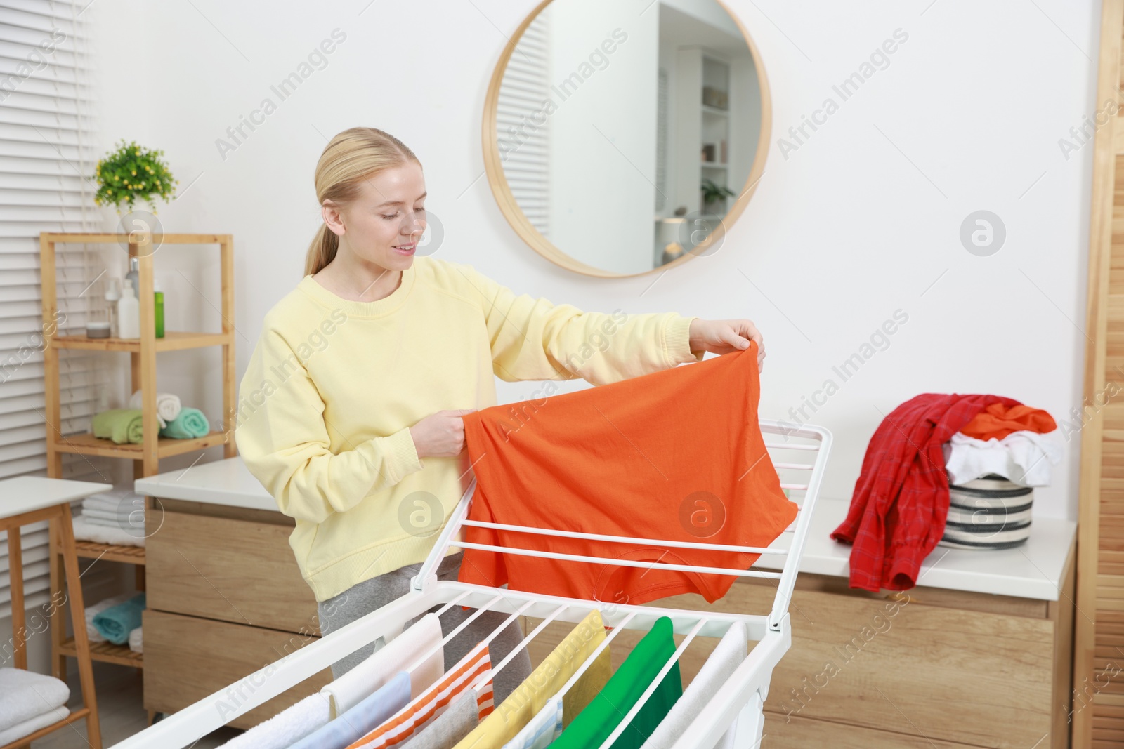 Photo of Beautiful woman hanging fresh clean laundry on drying rack at home