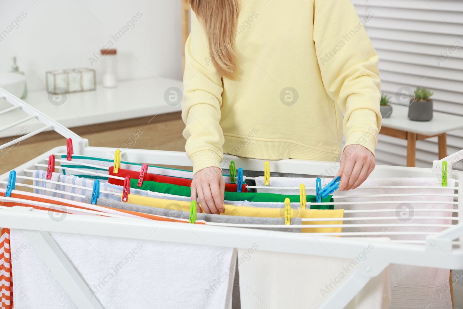 Photo of Woman hanging fresh clean laundry on drying rack at home, closeup