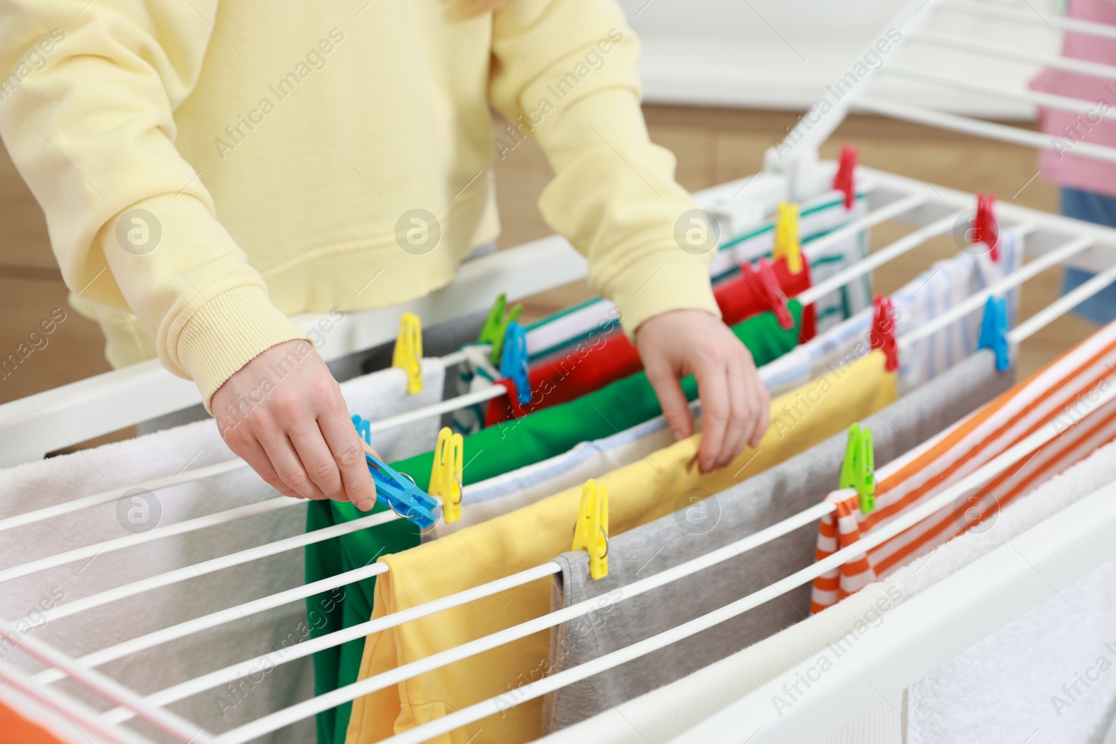 Photo of Woman hanging fresh clean laundry on drying rack at home, closeup