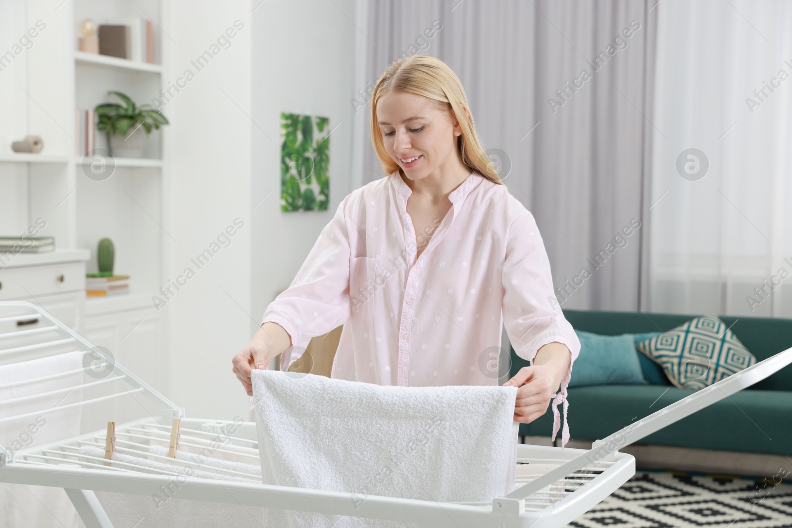 Photo of Beautiful woman hanging fresh clean laundry on drying rack at home