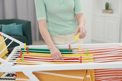 Photo of Woman hanging fresh clean laundry on drying rack at home, closeup