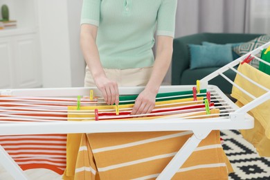 Photo of Woman hanging fresh clean laundry on drying rack at home, closeup