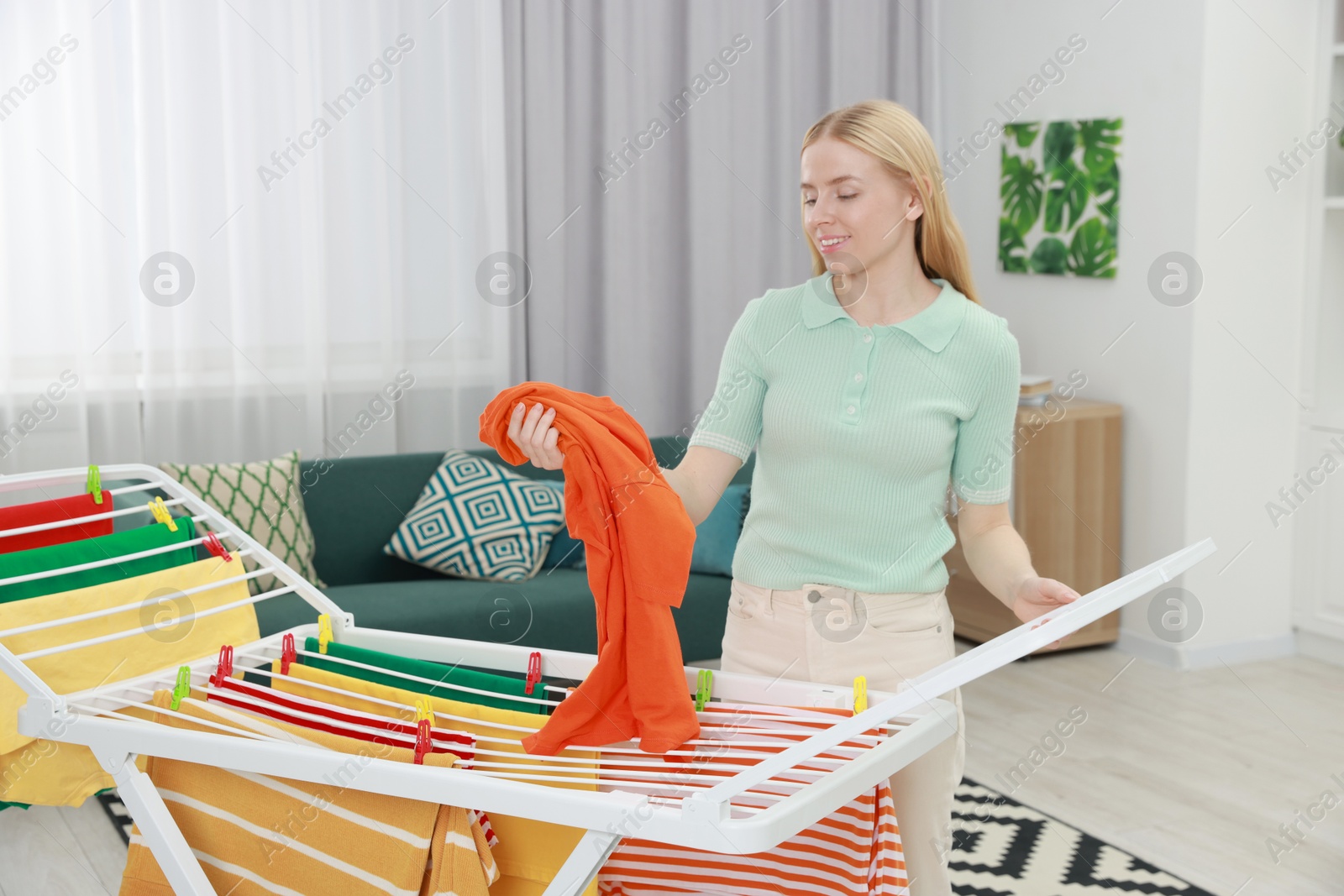 Photo of Beautiful woman hanging fresh clean laundry on drying rack at home