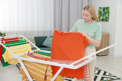 Photo of Beautiful woman hanging fresh clean laundry on drying rack at home