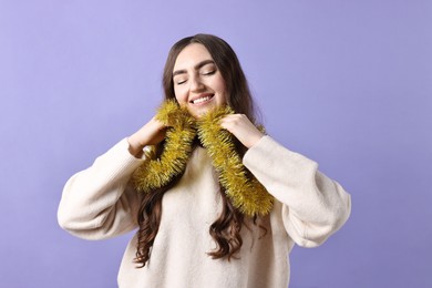 Happy young woman with tinsel on purple background