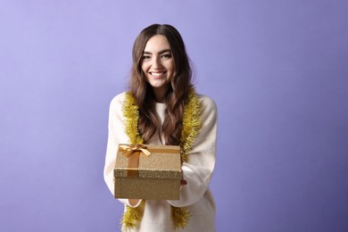 Photo of Happy young woman with tinsel and gift box on purple background