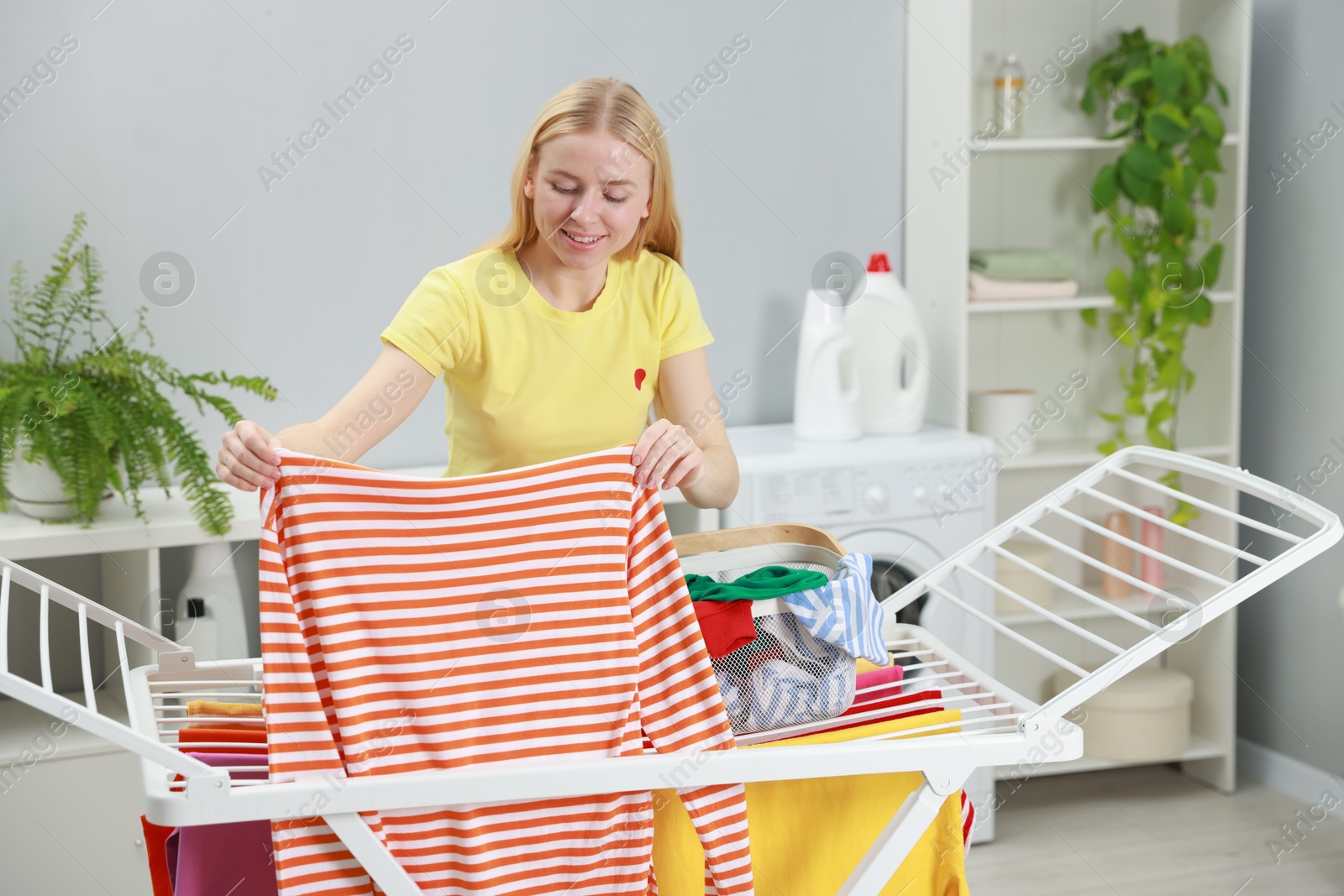 Photo of Beautiful woman hanging fresh clean laundry on drying rack at home