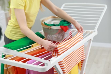 Woman hanging fresh clean laundry on drying rack at home, closeup