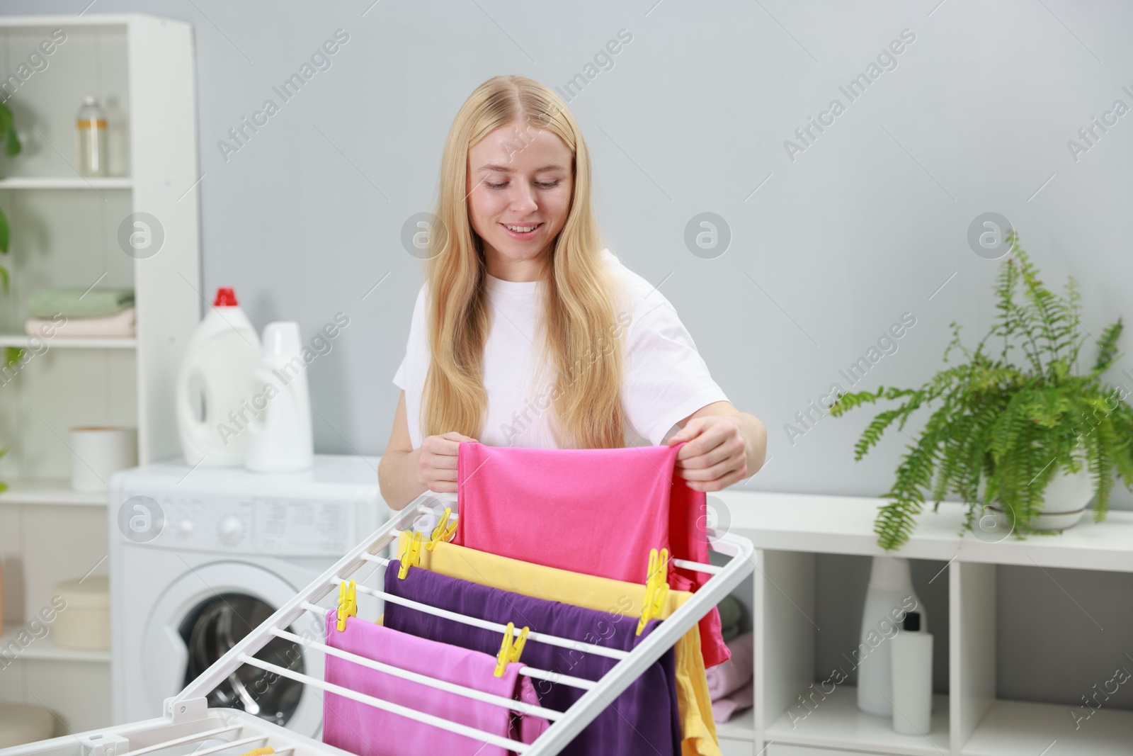 Photo of Beautiful woman hanging fresh clean laundry on drying rack at home