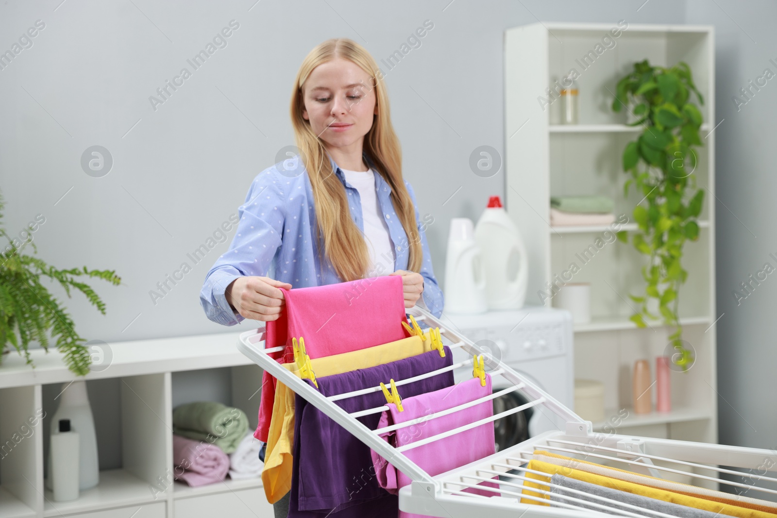 Photo of Beautiful woman hanging fresh clean laundry on drying rack at home