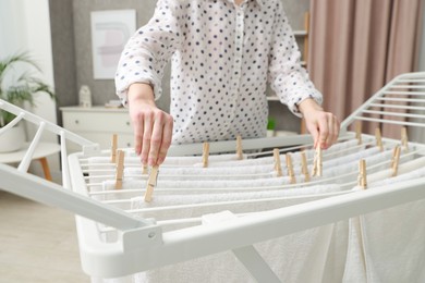 Woman hanging fresh clean laundry on drying rack at home, closeup