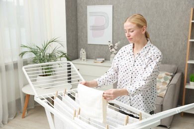 Beautiful woman hanging fresh clean laundry on drying rack at home