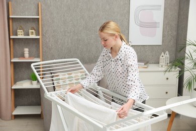 Beautiful woman hanging fresh clean laundry on drying rack at home