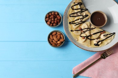 Photo of Delicious crepes with banana, nuts and chocolate sauce on light blue wooden table, flat lay. Space for text