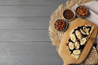 Delicious crepe with banana, nuts and chocolate sauce on grey wooden table, flat lay. Space for text