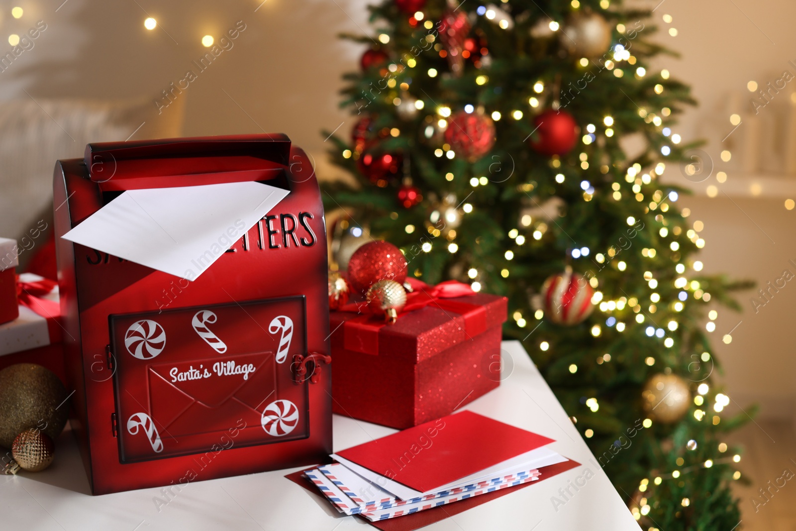 Photo of Santa Claus mailbox, letters, gift boxes and festive decor on table indoors. Christmas atmosphere