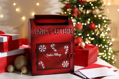 Photo of Santa Claus mailbox, letters, gift boxes and Christmas decor on white table indoors