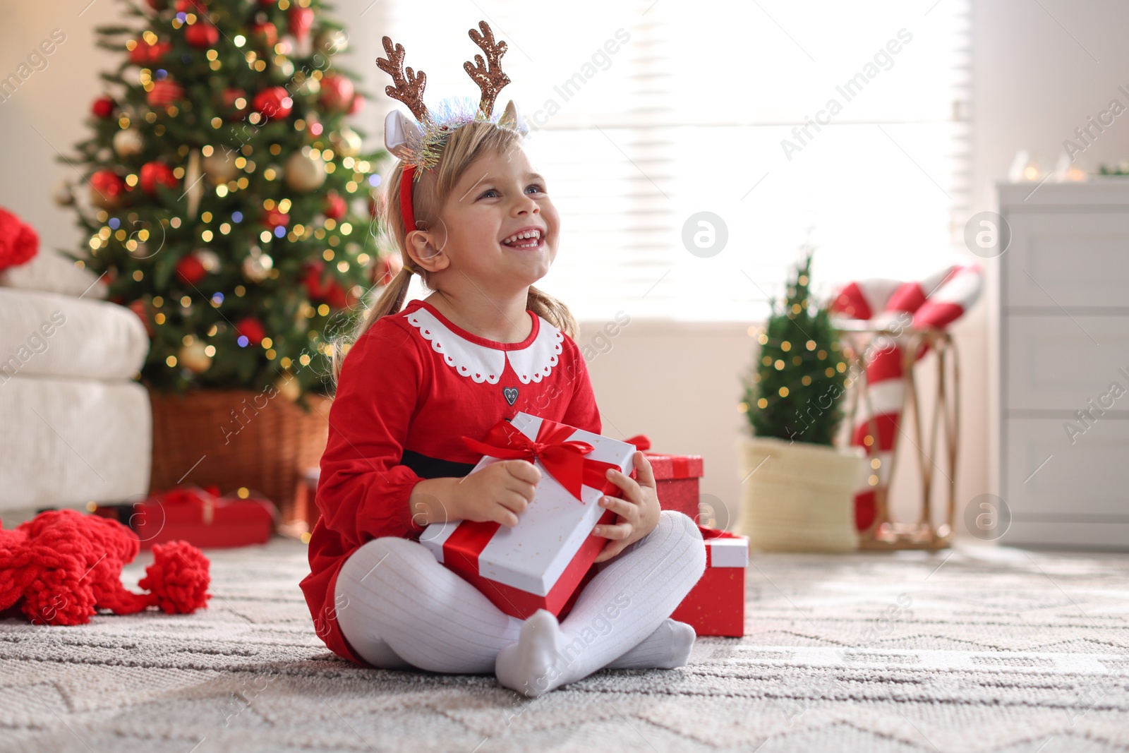 Photo of Little girl in Christmas costume with gift boxes at home