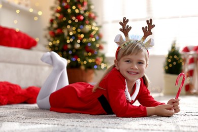 Photo of Little girl in Christmas costume with candy cane lying on floor at home