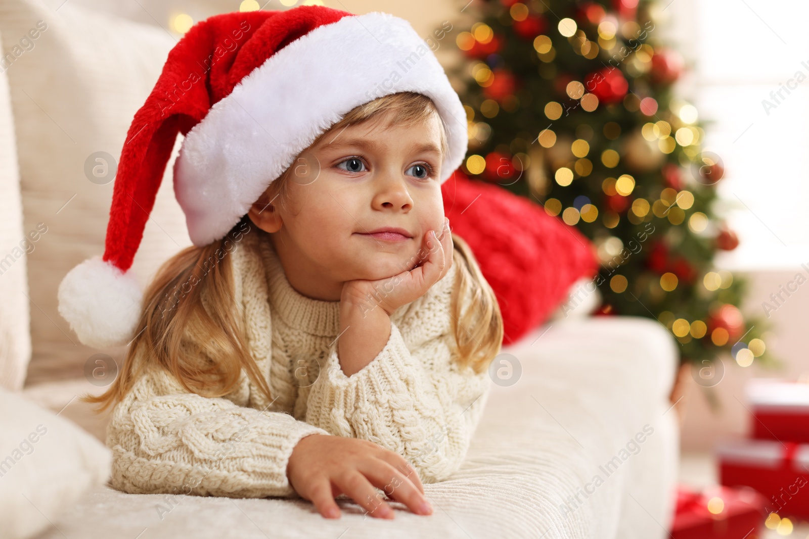 Photo of Little girl in Santa hat lying on sofa at home