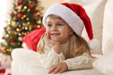 Photo of Little girl in Santa hat lying on sofa at home