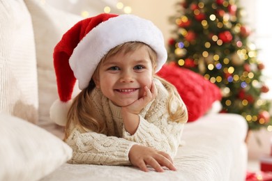 Photo of Little girl in Santa hat lying on sofa at home