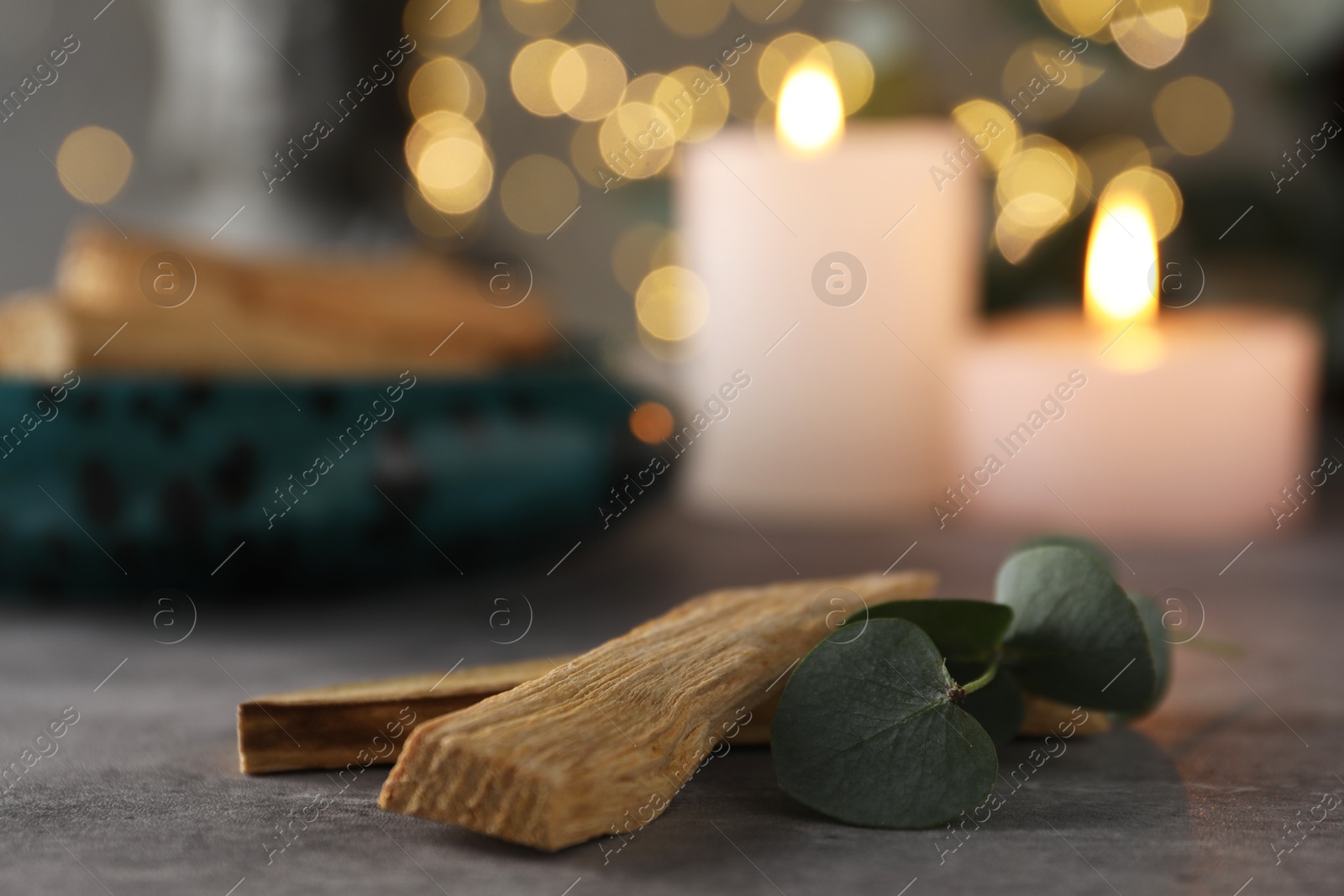 Photo of Palo santo sticks, eucalyptus leaves and burning candles on grey table, closeup