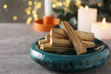 Photo of Palo santo sticks and burning candles on grey table, closeup. Space for text