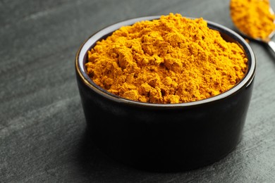 Photo of Turmeric powder in bowl on grey table, closeup