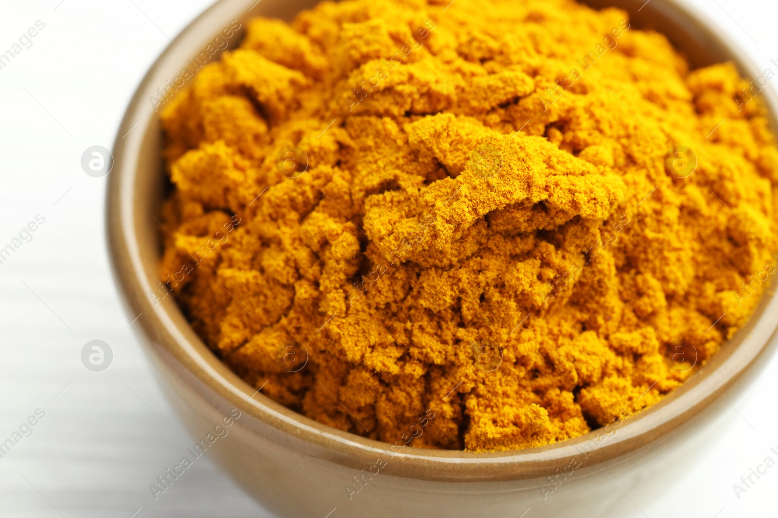 Photo of Turmeric powder in bowl on white table, closeup