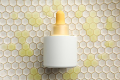 Bottle of skin care product on beige honeycomb surface, top view