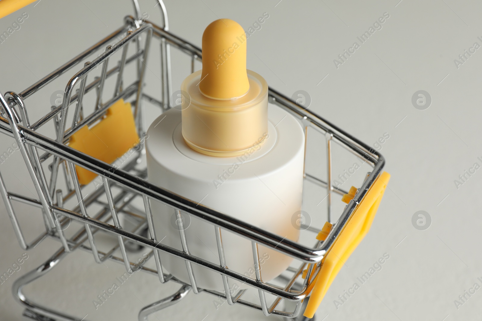 Photo of Bottle of skin care product in small shopping cart on light background, closeup